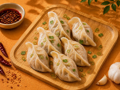 Cooked peppered beef dumplings on a wooden board with chilli oil, coriander and spring onion