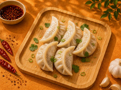 Cooked chicken and chive dumplings on a wooden board with chilli oil, coriander and spring onion