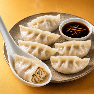 Chicken and chive dumplings on a plate with dipping sauce, one open on a spoon showing the filling